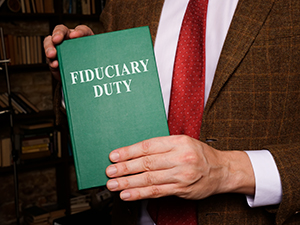a man dressed in a suit but no face shown is holding a green book with text stating “fiduciary duty”.