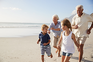 Two grandparents running on the beach with their two grandchildren.